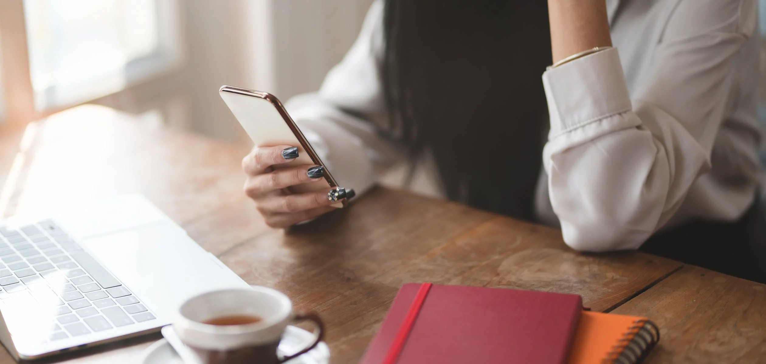 Stock image of someone on their phone while sitting at a desk with a laptop